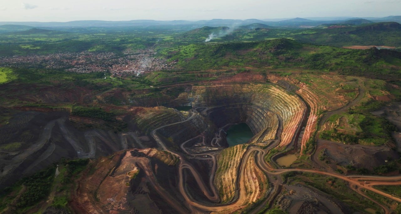 Drone view of an open-pit gold mine among green hills in Guinea, West Africa, filmed for a Nordgold corporate film
