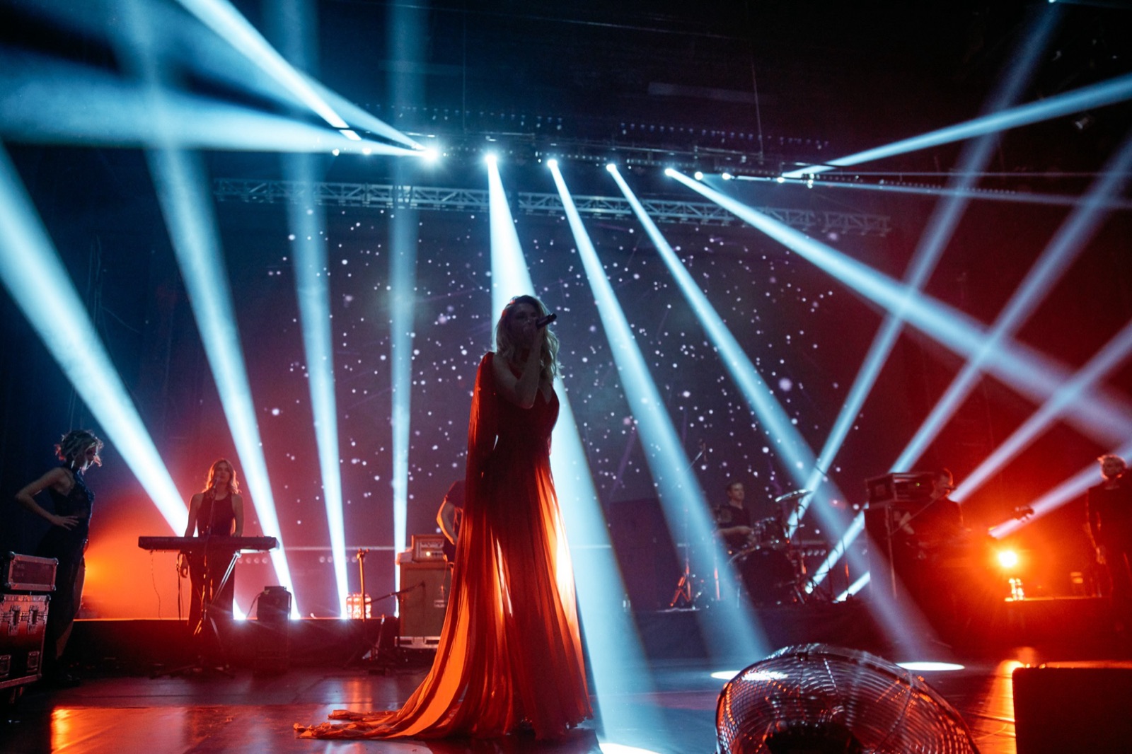 Private event show: a singer in a long red gown on stage, cut through by beams of light