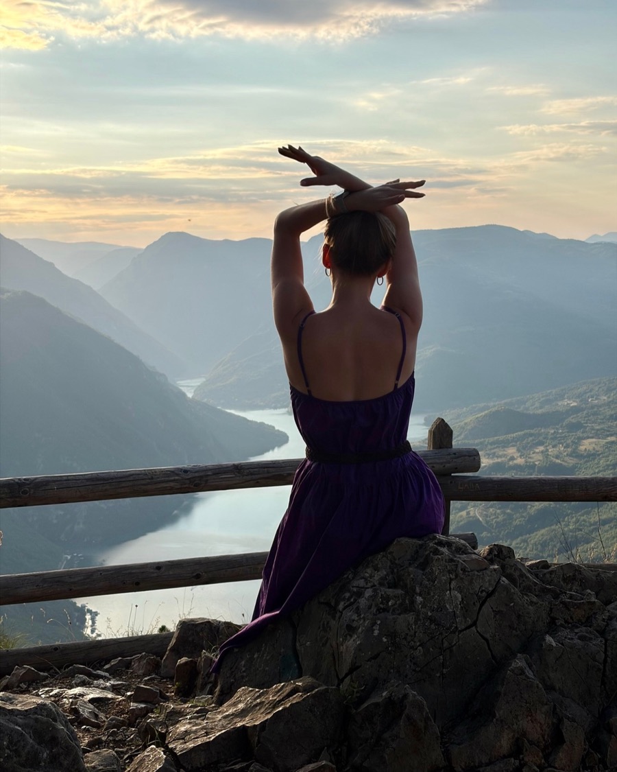 Masha from behind, arms raised, on a mountain lookout above a river canyon in Serbia at sunset