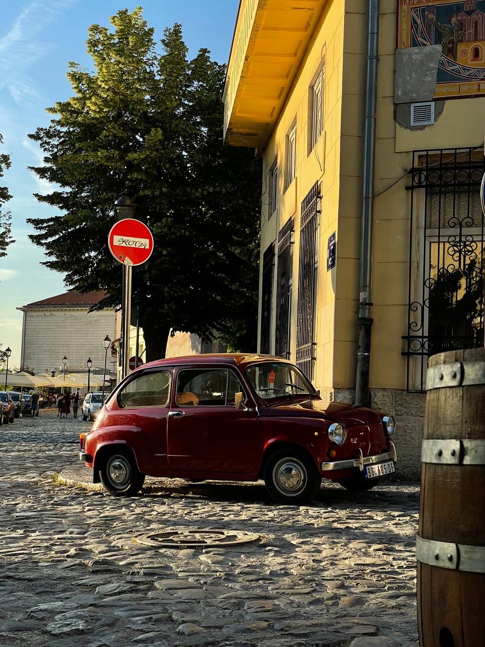A vintage red Fiat on a cobbled street in Belgrade’s old town at golden hour