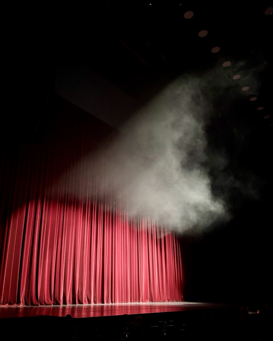 A theatre stage with a red curtain and stage smoke in a beam of light